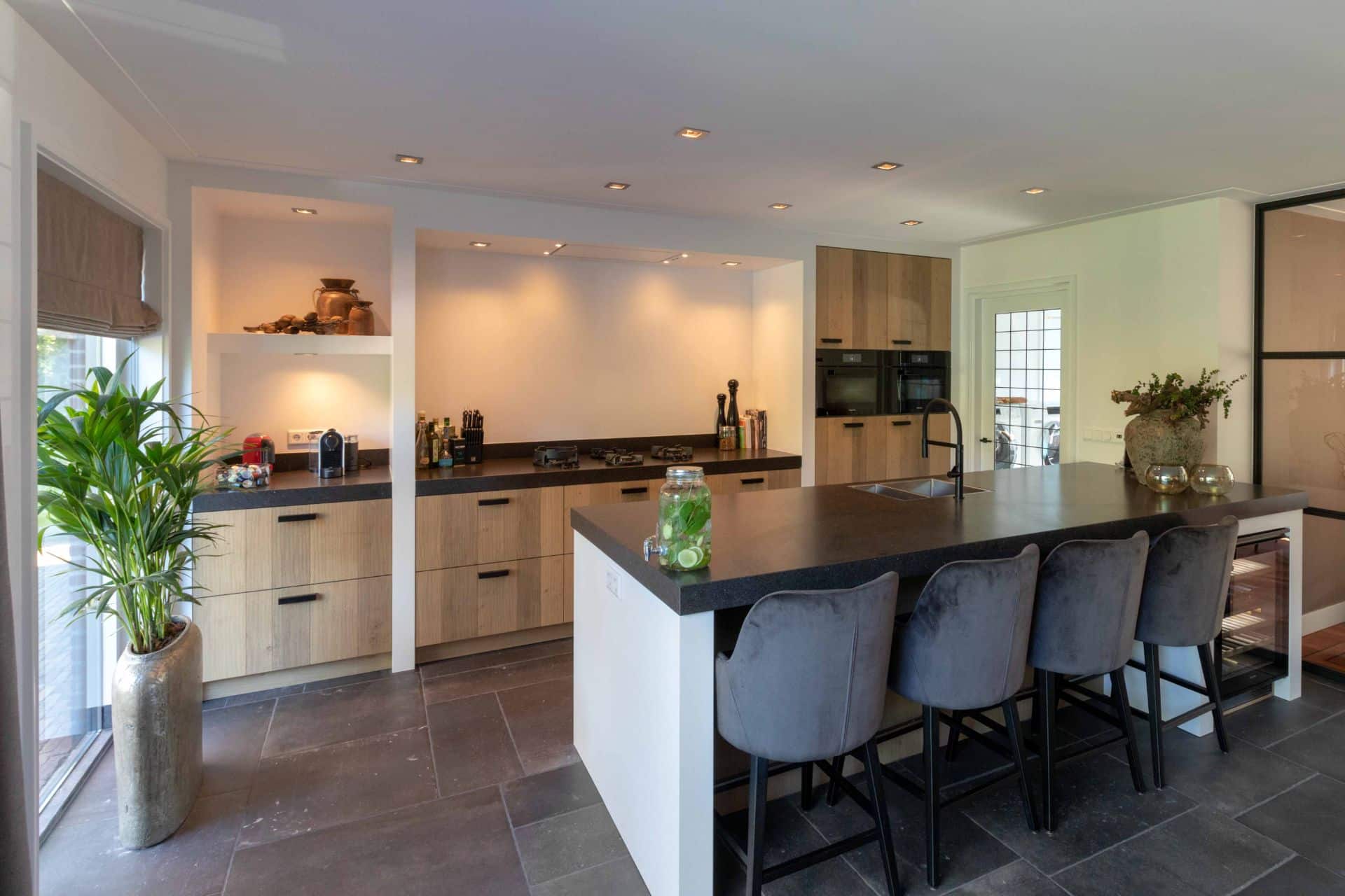 Landelijke keuken met houten kasten, een kookeiland met zwarte afwerking, en sfeervolle inbouwverlichting.