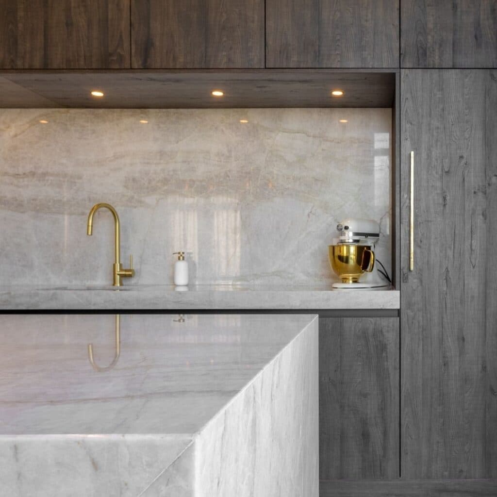 Impressie van een luxe keuken, voorzien van een kookeiland en keuken nis in glanzend marmer met gouden aders.