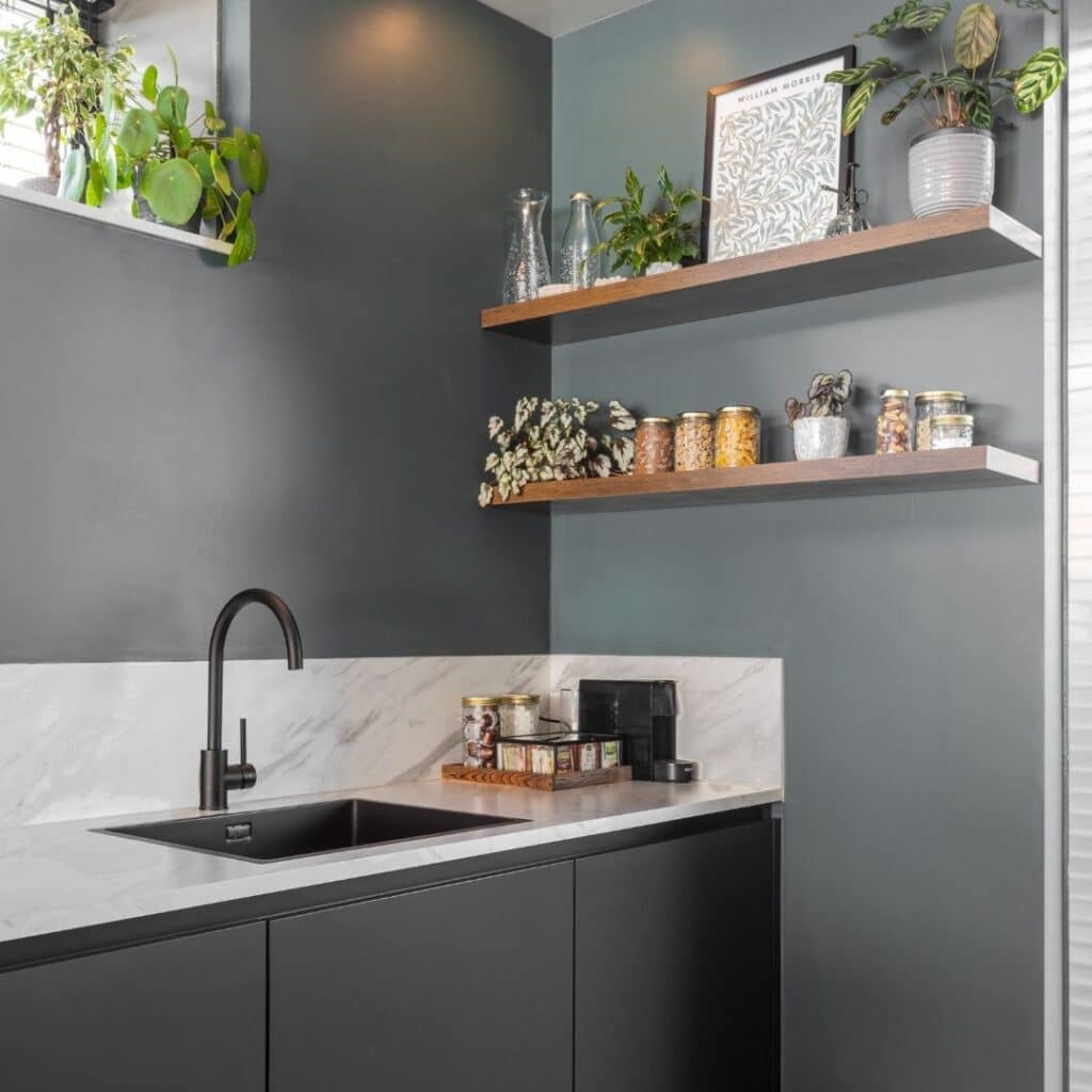 Impressie van een moderne keuken met een natuursteenlook wit blad en spatwand, zwarte onderkasten en zwarte Quooker.