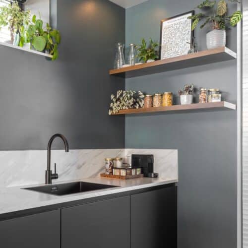 Impressie van een moderne keuken met een natuursteenlook wit blad en spatwand, zwarte onderkasten en zwarte Quooker.