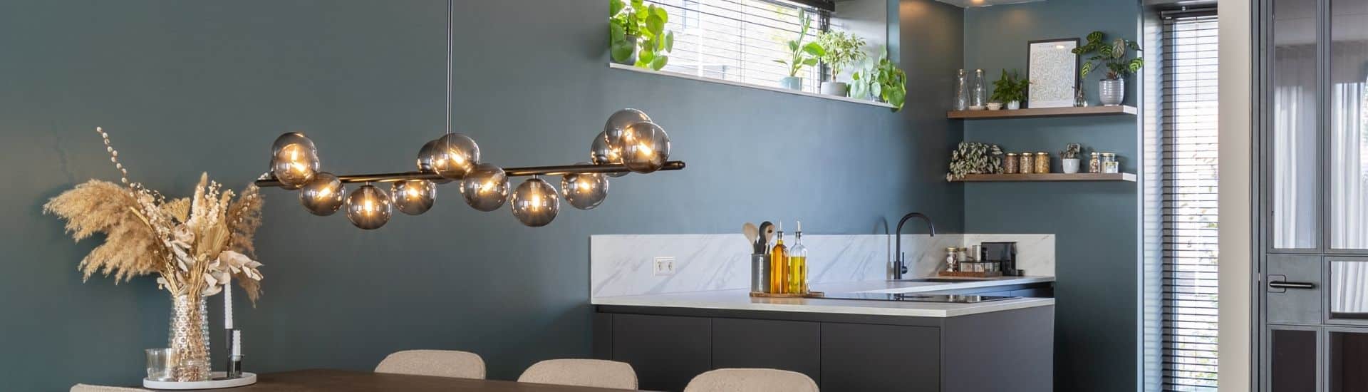 Impressie van een moderne keuken met hoekopstelling. De keuken is voorzien van zwarte kasten en een natuursteenlook werkblad in wit. Het blad loopt een stukje door op de groene wand.