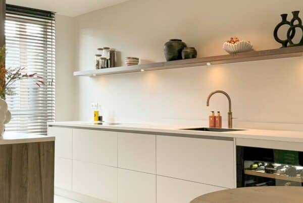 Impressie van een Japandi keuken in een parallel opstelling. De keuken is ingericht met een strak werkblad, veel opberglades, een Quooker, een wijnklimaatkast en houten kastenwand.