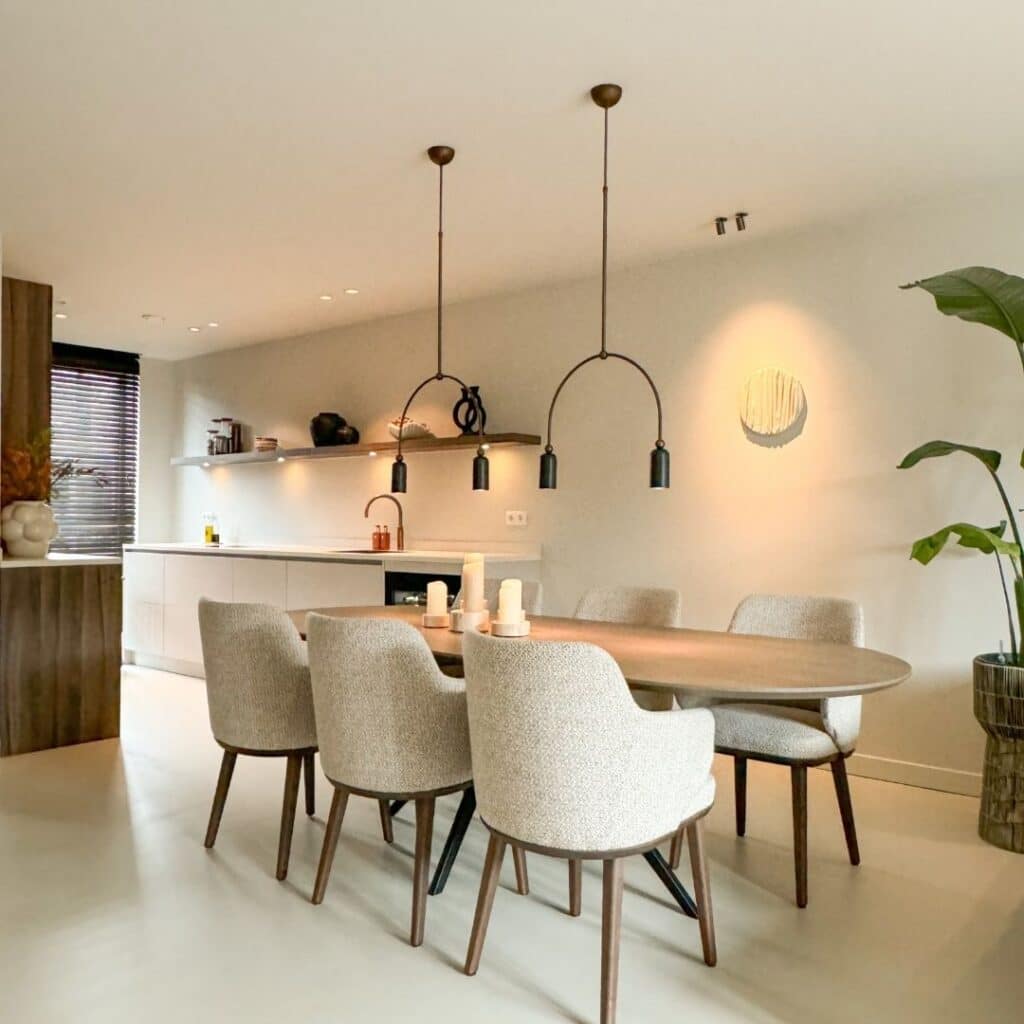 Impressie van een benedenverdieping met een Japandi keuken in een parallel opstelling. De keuken is ingericht met een strak werkblad, veel opberglades, een Quooker, een wijnklimaatkast en houten kastenwand.