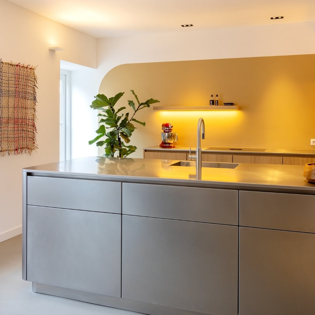 Impressie van een design keuken, voorzien van een volledig RVS schiereiland. Het eiland heeft lades aan de lange zijden en is voorzien van een design wasbak met Quooker.