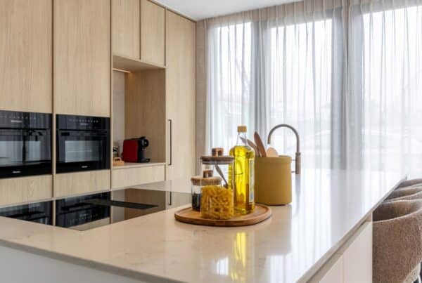 Impressie van een Japandi stijl keuken met kookeiland, natuursteenlook werkblad en licht eiken kastenwand met inbouw ovens.