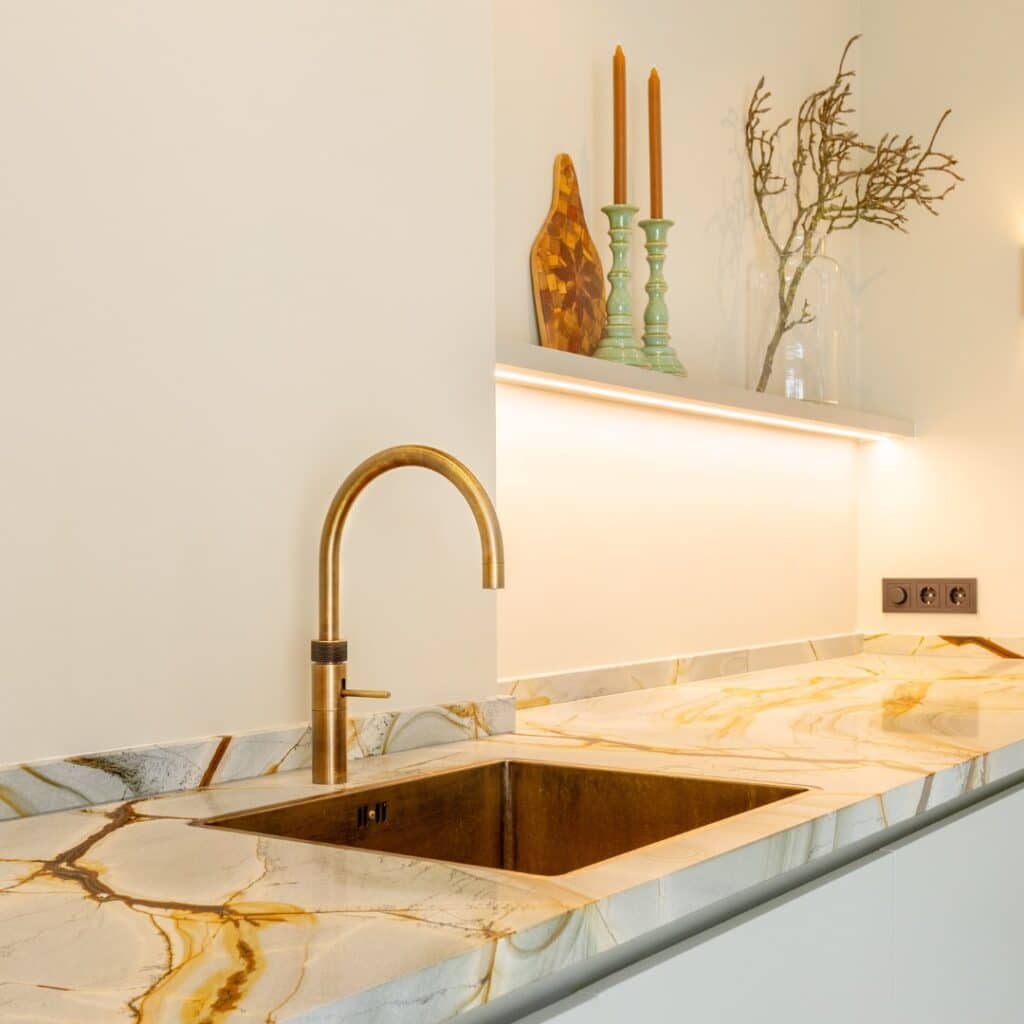 Impressie van een luxe keuken met rustige kleuren, voorzien van marmer werkblad, design wasbak en kraan in geborsteld messing.