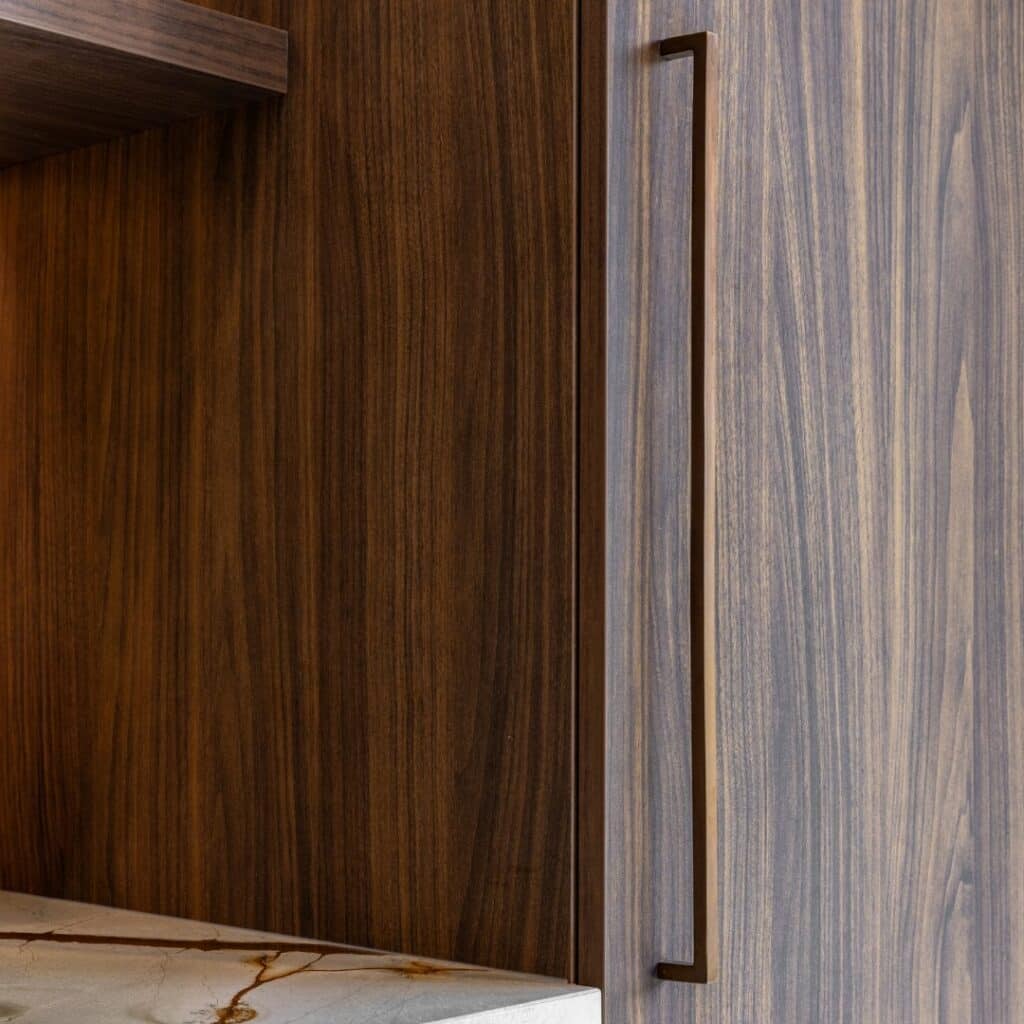 Close-up van een notenhouten kast, met een nis met marmer werkblad en kastdeur met handgreep in warme aardetint.