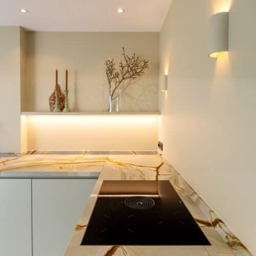 Impressie van een luxe keuken met rustige kleuren, voorzien van marmer werkblad en kookplaat met werkbladafzuiging.