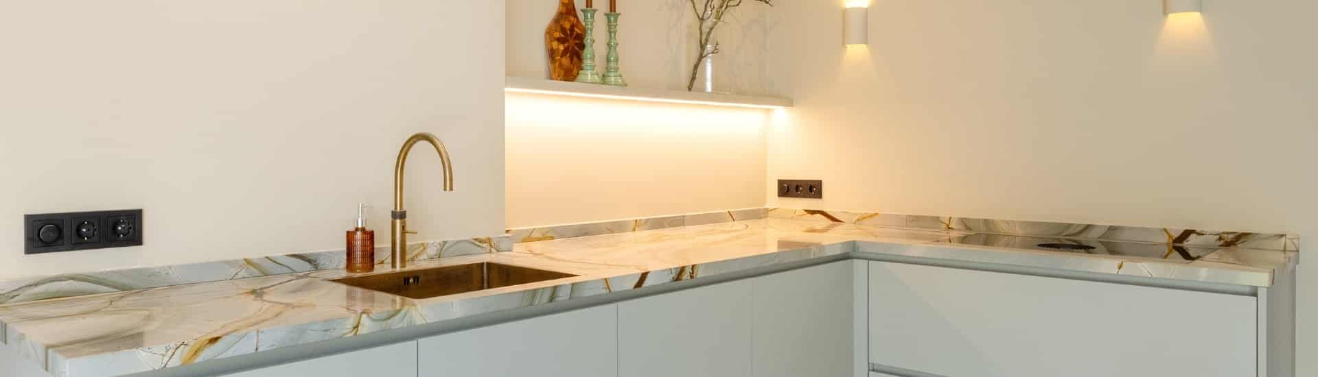 Impressie van een luxe keuken in hoekopstelling, voorzien van marmer werkblad en kraan in geborsteld messing.