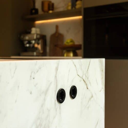 Close-up van een zijwand van een kookeiland. De wand is wit, met een zwart marmer patroon.