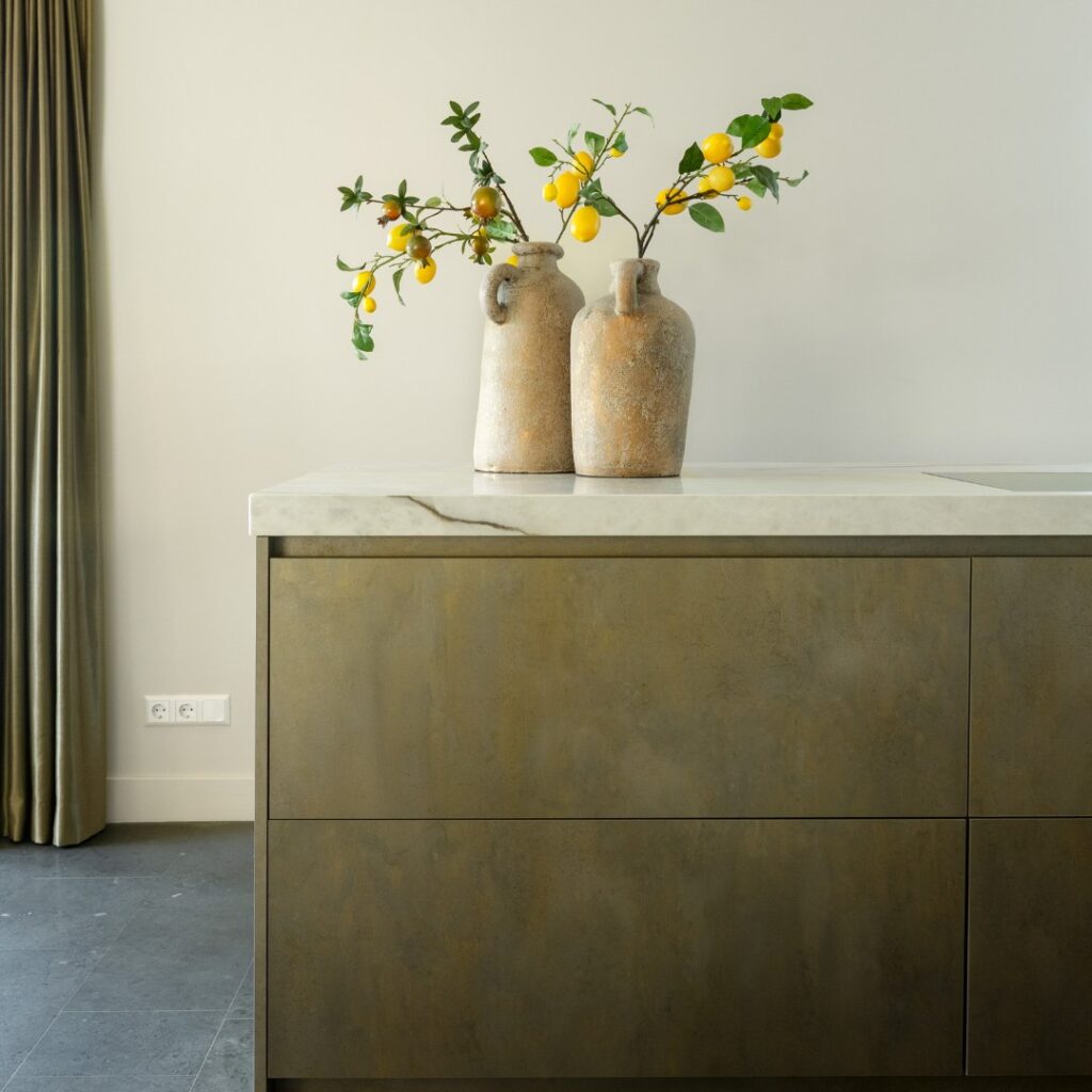 Impressie van een kookeiland met marmerlook werkblad en grijsgroene lades in een verweerde look.