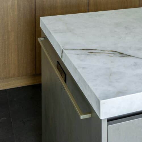 Close-up van bovenaf van een deel van een kookeiland, met een marmerlook blad, verweerd groengrijze zijdes en handdoekhouder.