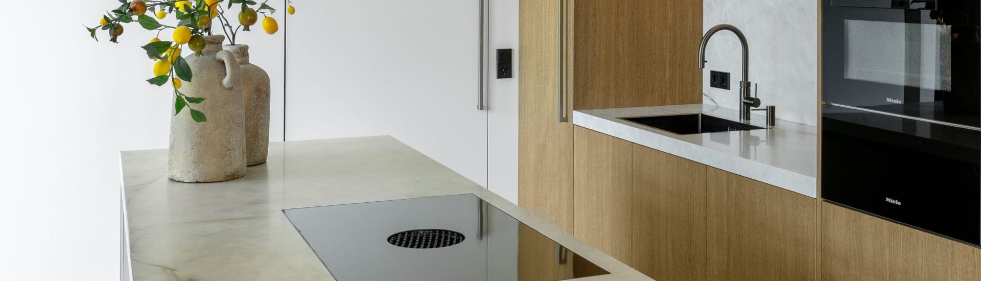 Impressie van een keuken met licht eiken kastenwand en kookeiland met marmerlook blad en kookplaat met werkbladafzuiging.