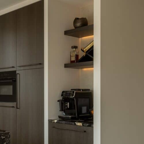 Impressie van een houten kastenwand, met daarnaast een nis met een koffiecorner.