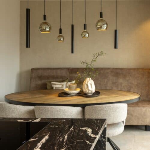 Hotel Chique leefruimte, voorzien van zithoek met ovale houten tafel, bank en drie stoelen. We kijken ernaar vanuit een moderne keuken met zwart marmerlook kookeiland.