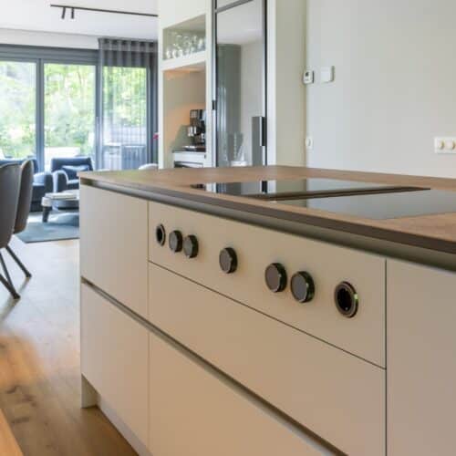 Impressie van een strak kookeiland met witte lades en een zwart werkblad. Het eiland is voorzien van een Bora kookplaat met werkbladafzuiging.