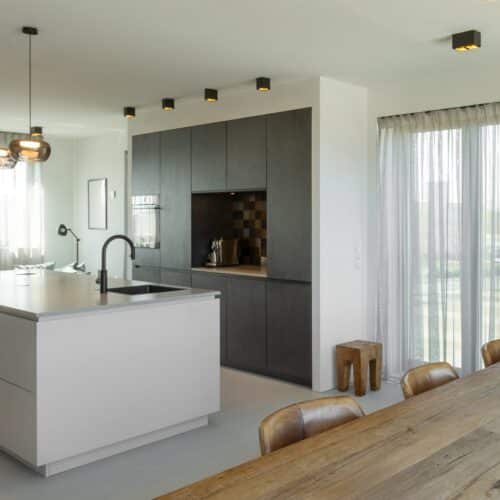 Impressie van een woonkamer met in het midden een zwart-wit keuken met kookeiland.