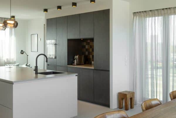 Impressie van een woonkamer met in het midden een zwart-wit keuken met kookeiland.