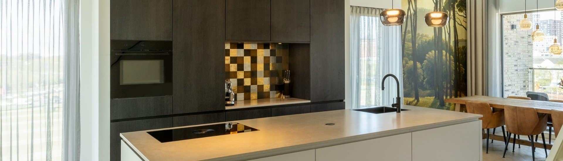 Impressie van een woonkamer met in het midden een zwart-wit keuken met kookeiland.